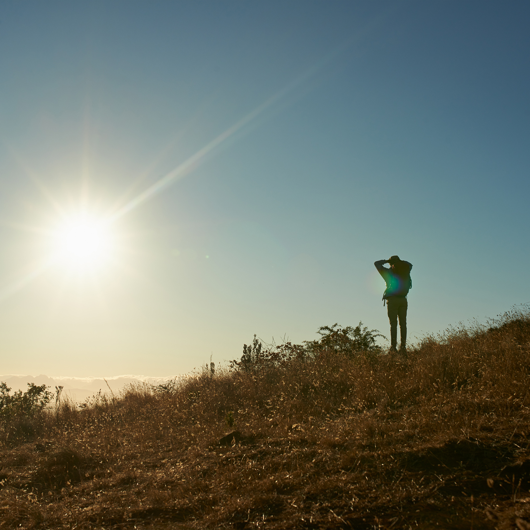 Woman hiker stands on slope viewing the sun over ocean