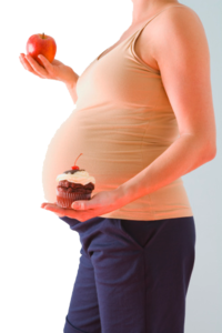 Pregnant woman holding apple in one hand and cupcake in the other