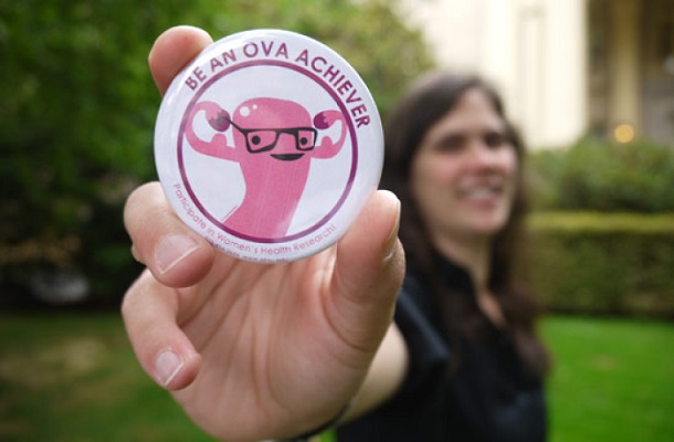 Out of focus woman holds in-focus "ova achiever" button up to camera