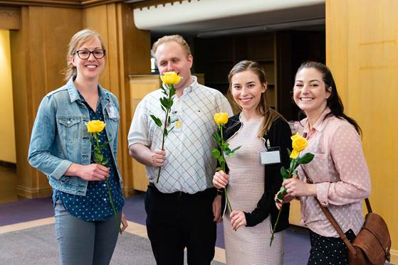 Four young interns and staff involved in the program pose with gold roses