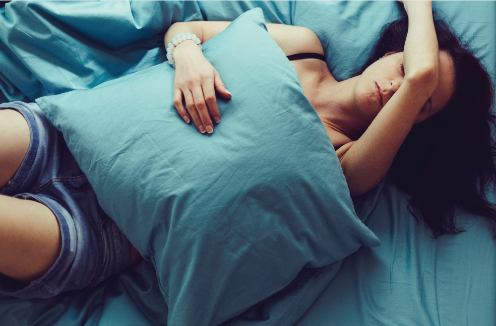 woman lies on blue sheets hugging pillow