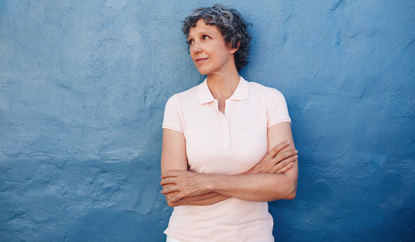 Woman stands with arms crossed in front of blue wall