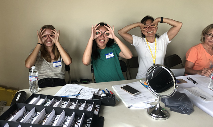 Volunteers have fun making eye glasses with the hands as they help provide free eye screenings to participants