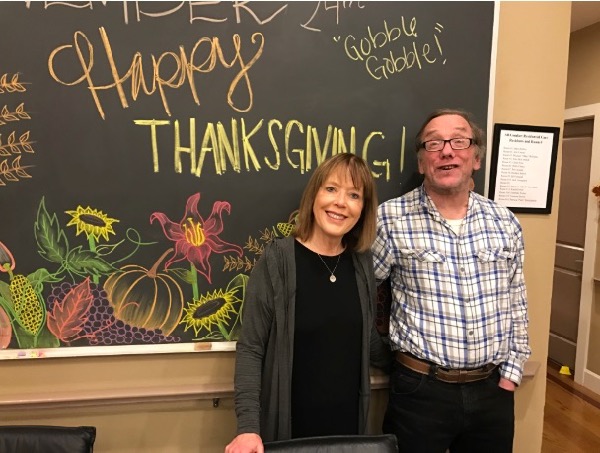 Kate and her husband, Glenn, stand in front of a blackboard that says "Happy Thanksgiving"