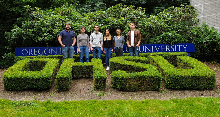 Pruneda Lab researchers stand outside in front of an Oregon Health & Science University sign, behind bushes trimmed to spell, "OHSU."