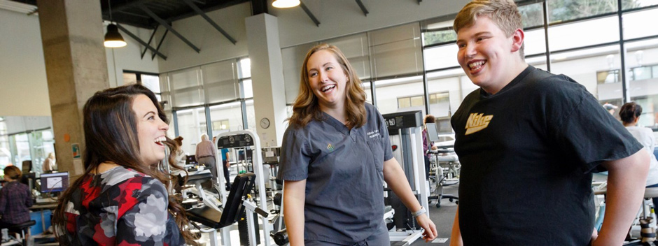 Will Van Dyke (right) with physical therapist Sarah Staropoli (left) and physician assistant Alissa Lyman (center) with workout equipment in the background.