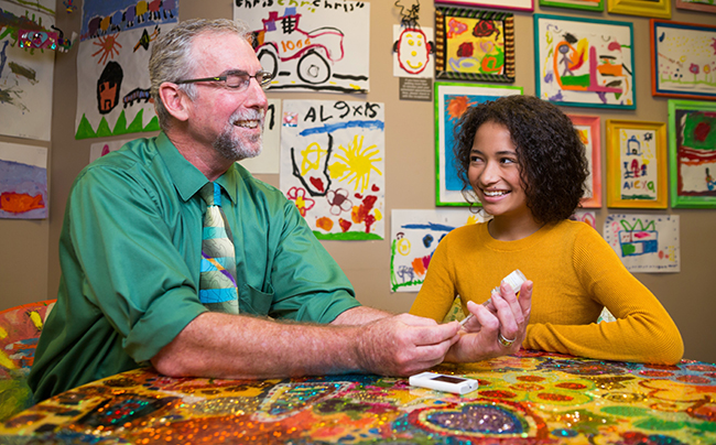 Dr. Michael Harris sitting at a table with a young girl giving a tutorial on how to give yourself an insulin injection.