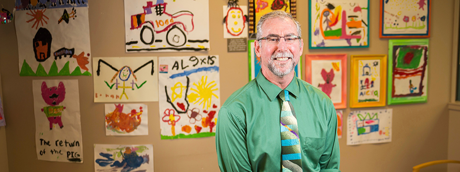 Dr. Michael Harris, Director for OHSU Doernbecher Children's Hospital's NICH Program, smiling in front of a wall with several kids' drawings.