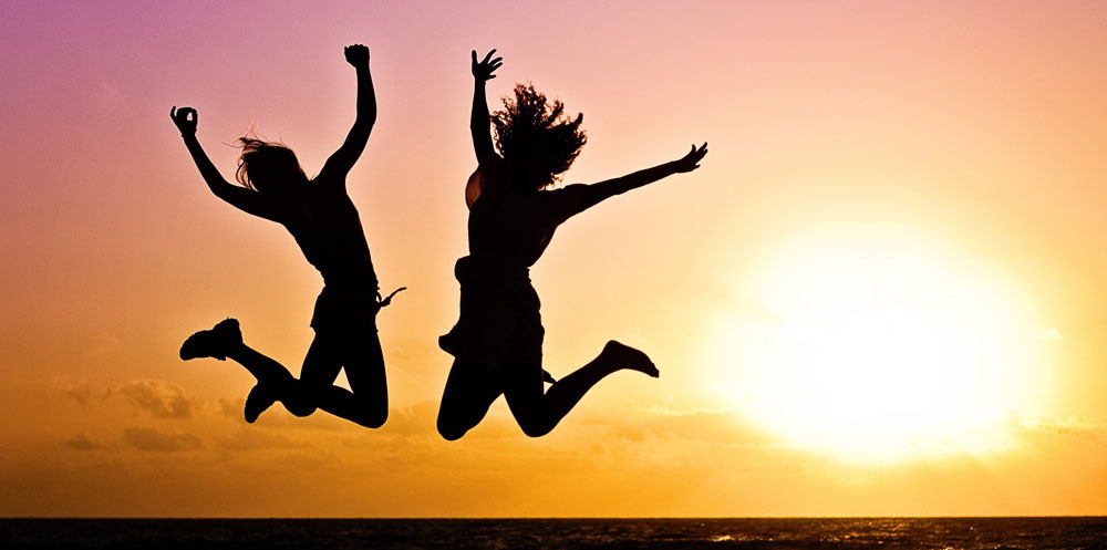 two people jumping on a beach silhouetted against a sunset