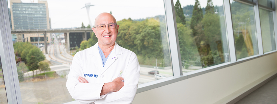 A male doctor standing arms-crossed in front of a window in OHSU's Collaborative Life Sciences Building.