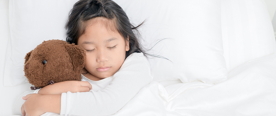 A little girl cuddling a teddy bear while sleeping in bed.