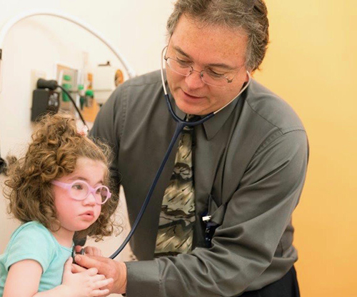A doctor uses a stethoscope to listen to a little girl's heart.