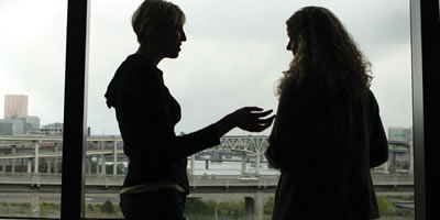 Two women talking in a hallway in silhouette standing next to a large window