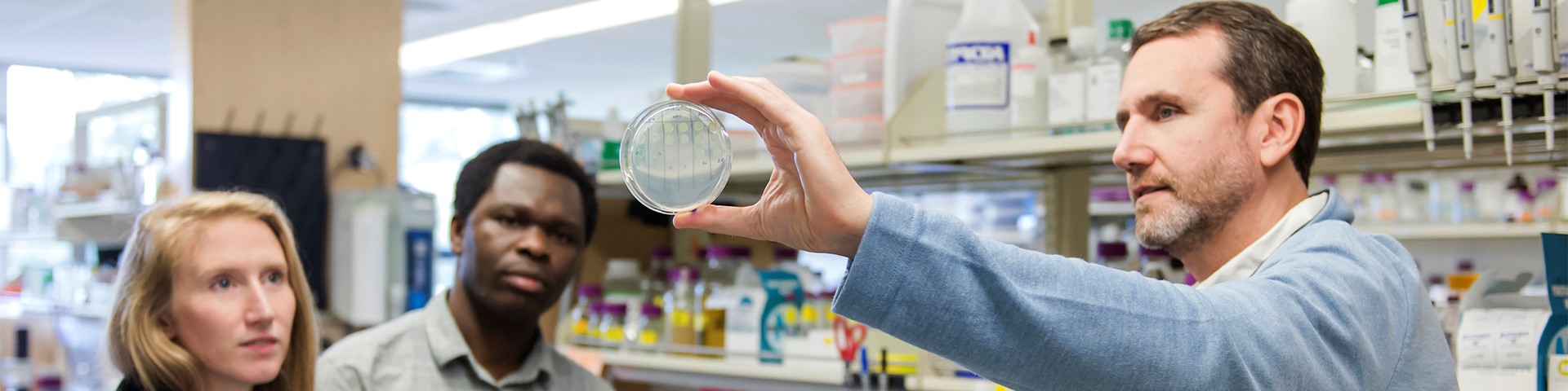 Image of faculty showing students a petri dish. 