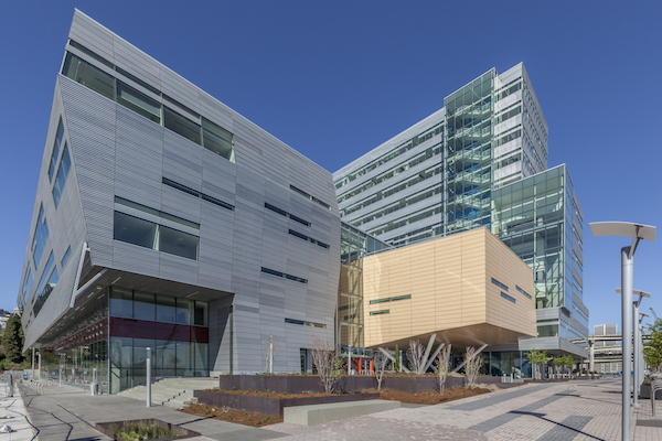 Modern building with silver, wood, and glass siding sits in front of a blue sky.