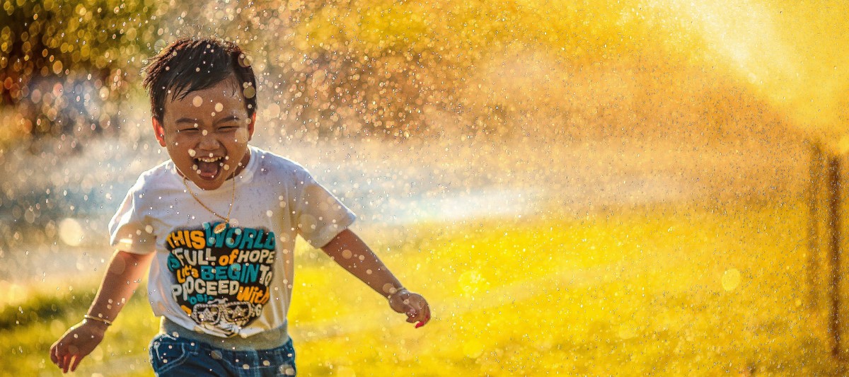 Boy laughing and running through the spray of a sprinkler