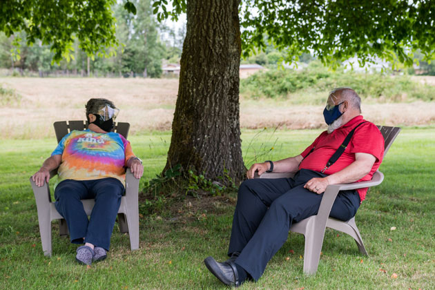 Family relaxing outside with faceshields on, socially-distancing