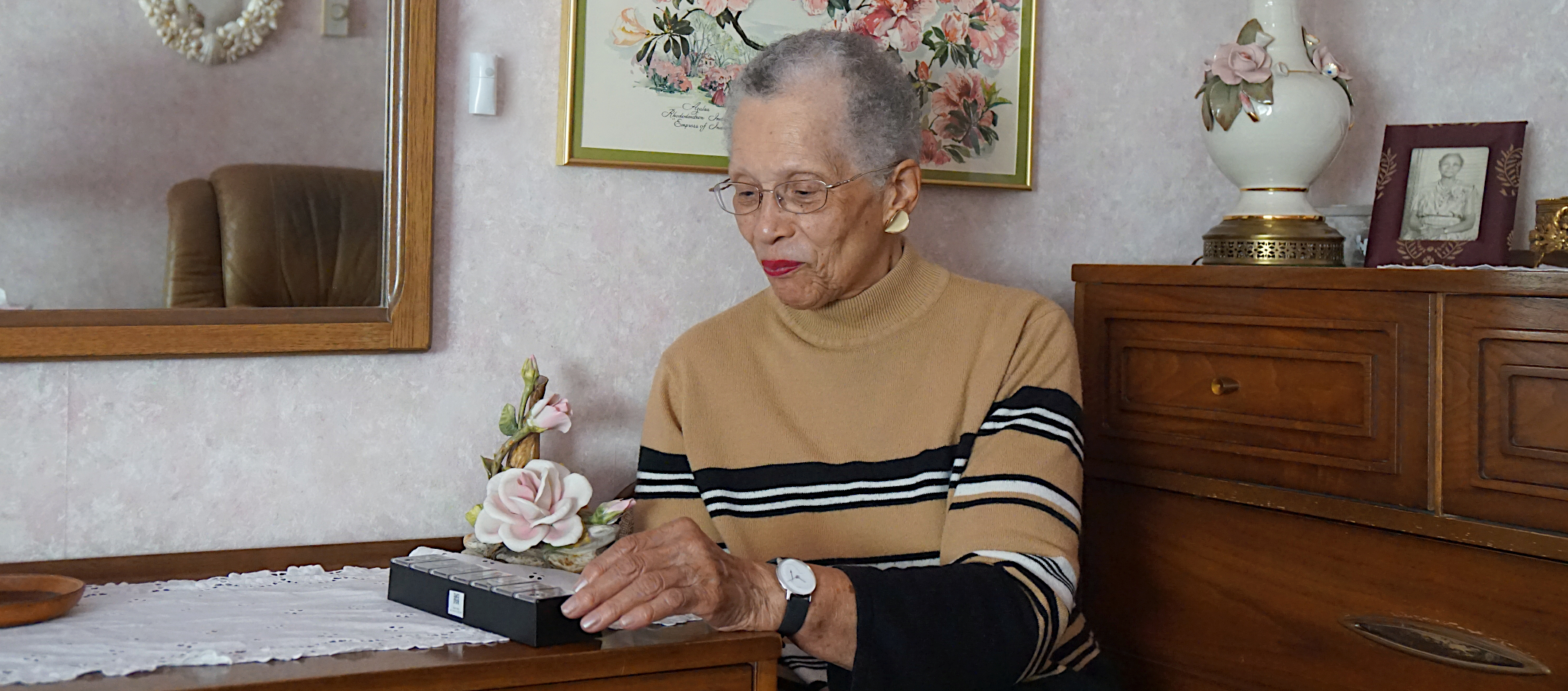 Older woman uses digital pillbox while sitting at desk 