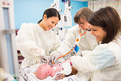 Three female OHSU providers smiling as they care for a newborn baby.