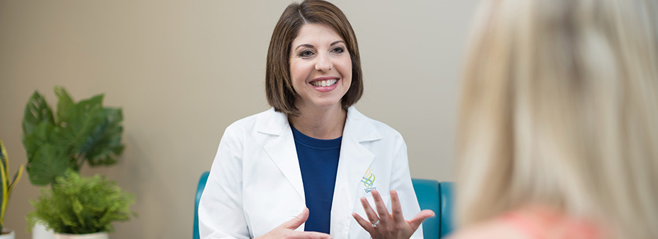 A female doctor sitting down smiling while providing an explanation to a female patient sitting across from her.