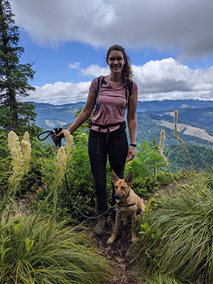 A woman smiling with her dog while on a hike.