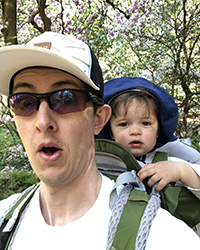 A man with his baby strapped to his back going on a walk outside.
