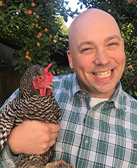 A photo of Michael Grubbs smiling while holding his pet chicken in his backyard.