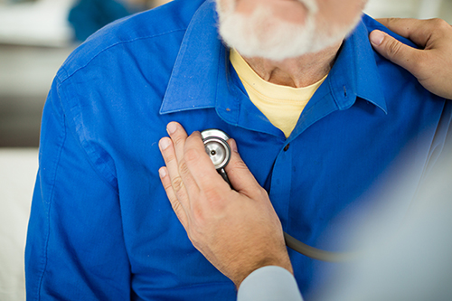 A doctor listening to an elderly man's heart using a stethoscope.