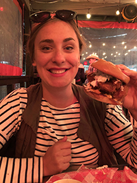 A woman smiling while out at a restaurant holding up a burger.
