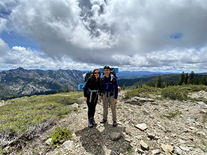 A man and a woman wearing hiking backpacks smiling while on a hike.
