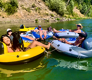 A group of people float in inter-tubes on a river on a sunny day.
