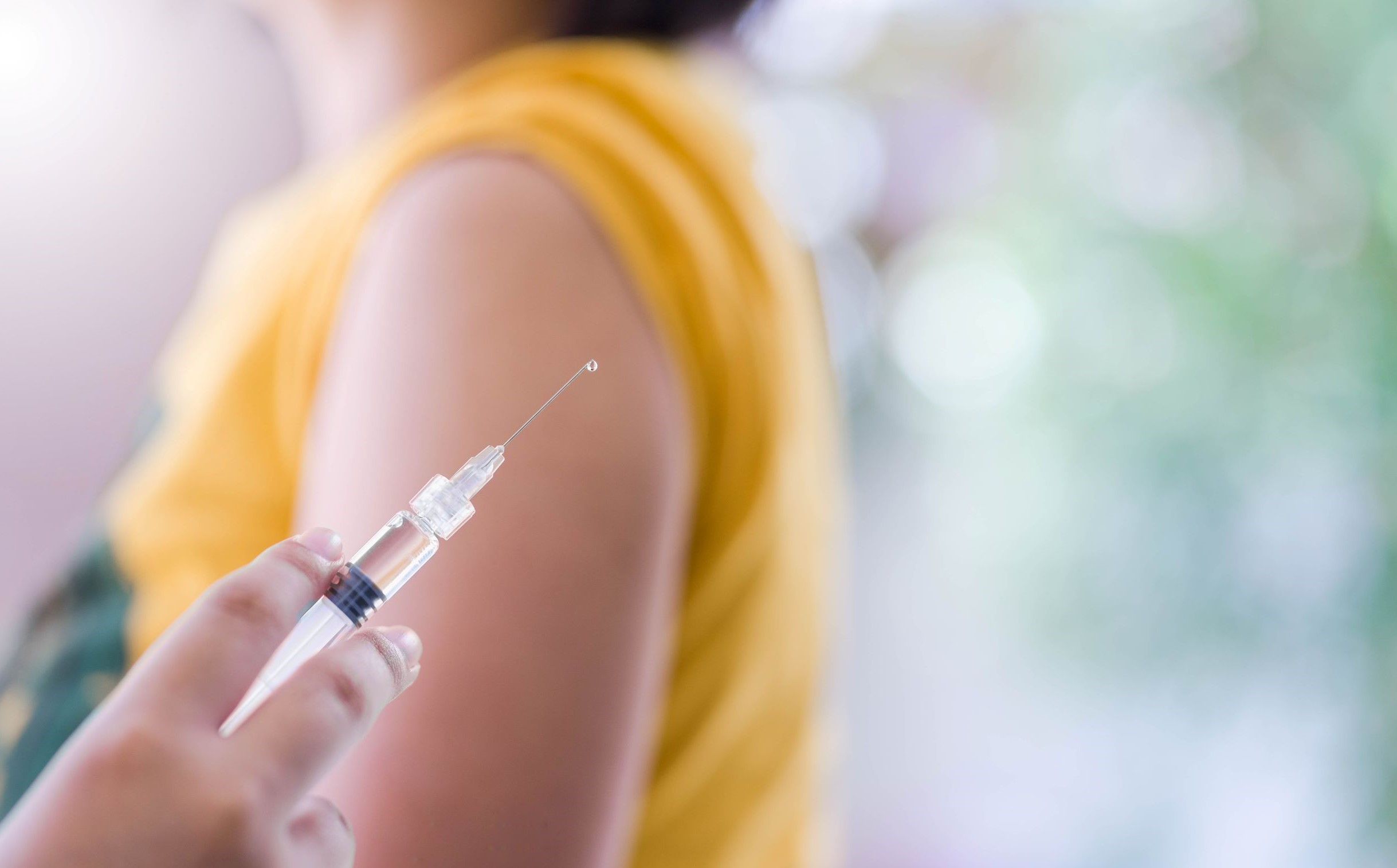 Blurry image of woman's arm with vaccination in foreground.