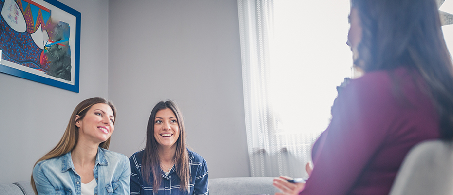 Couple sits on couch and listens to genetic counselor (seen from behind and below).