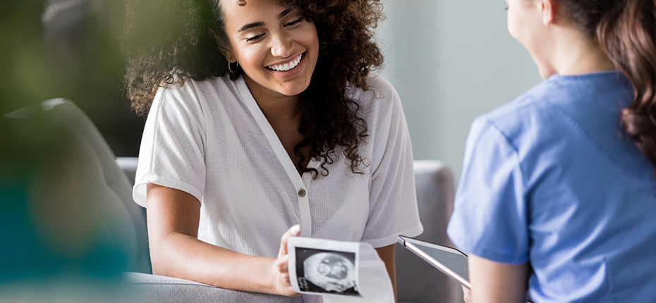 A smiling woman looks at an ultrasound image as she talks with her care provider.