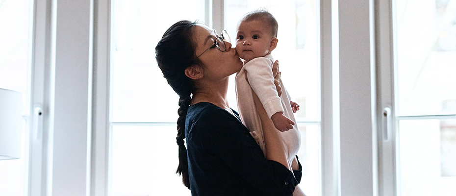 Asian woman holds up and kisses new baby