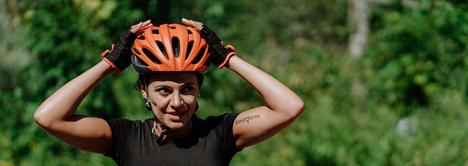 Woman puts on bike helmet on sunny day near the woods.