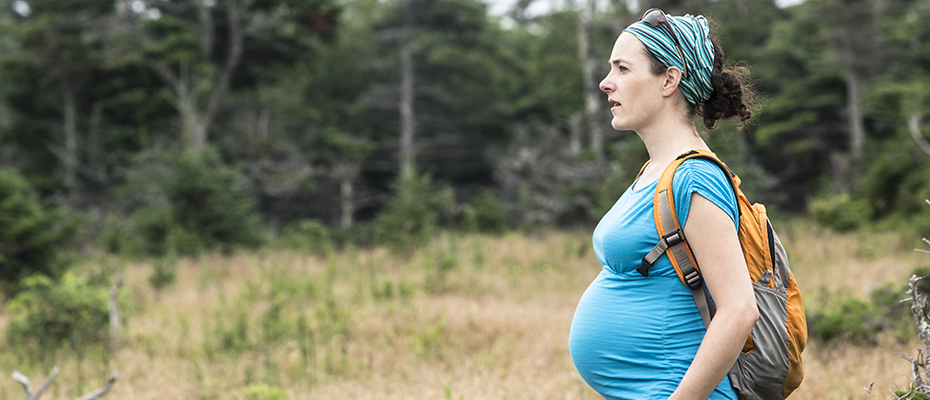 Pregnant woman wearing backpack on a trail in the woods