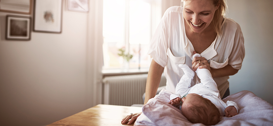 Mom smiles at baby and holds their foot as baby lays on blanket.