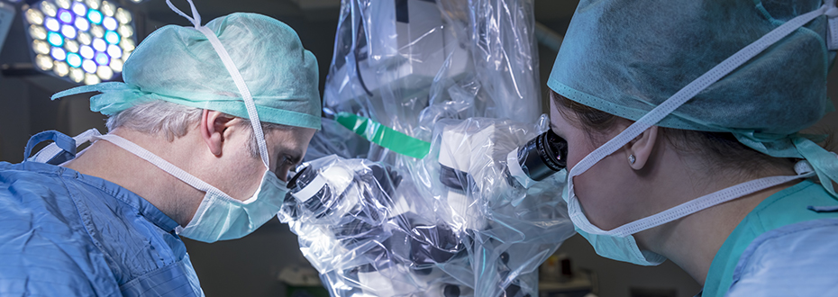 Two surgeons in masks and gowns operating robotic surgery device.