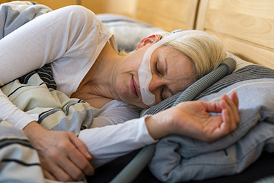 Stock photo of a person lying in a bed while wearing a CPAP machine for sleep apnea