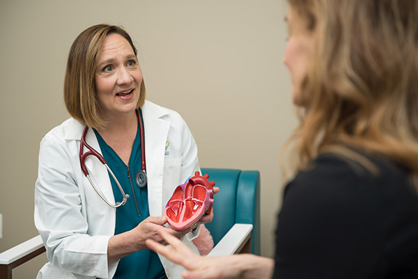 A female doctor sitting down speaking to a woman in a hospital exam room.