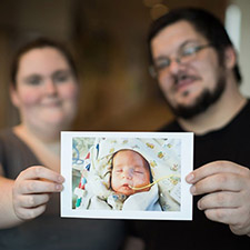 A woman and a man holding up a photo of a baby.