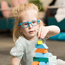 A little girl sitting on the floor playing with and stacking multi-colored blocks.