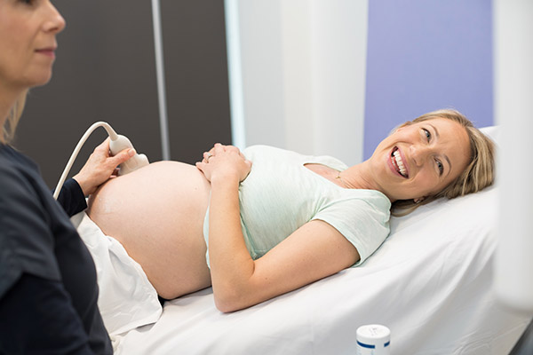Photo of a pregnant patient receiving a fetal scan and smiling