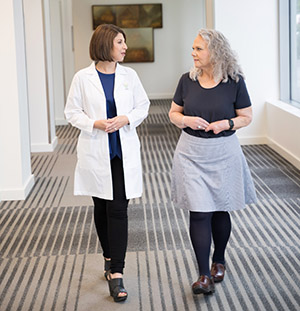 Two women walking down a hospital hallway talking to each other.