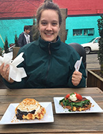 A photo of Clare Keddy sitting at an outdoor table of a restaurant with two plates of food in front of her.