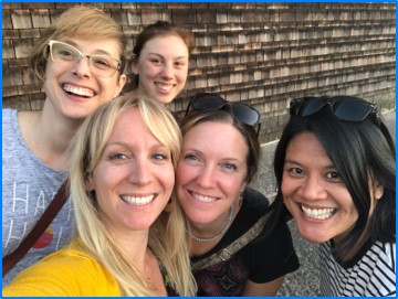 Five women of the Napier Lab at OHSU smile in a group selfie taken outside of a wooden shingled building