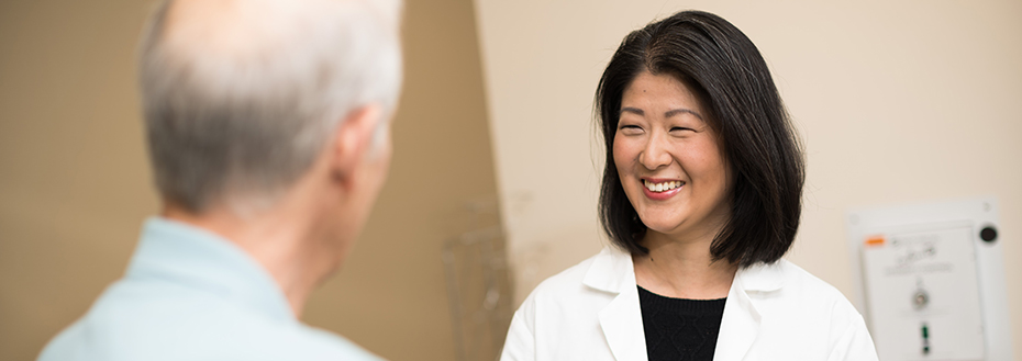 A female doctor smiling while speaking with an older man who is one of her patients.
