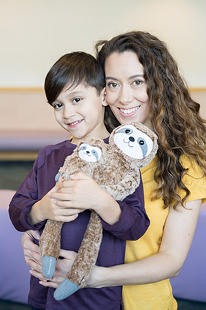Photo of a woman embracing a child who is holding stuffed toys of sloths