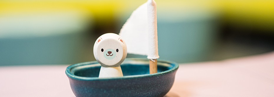 A smiling wooden toy bear sitting in a mini sailboat.
